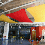 Solution acoustique pour un grand volume avec des voiles tendues de couleur rouge et jaune